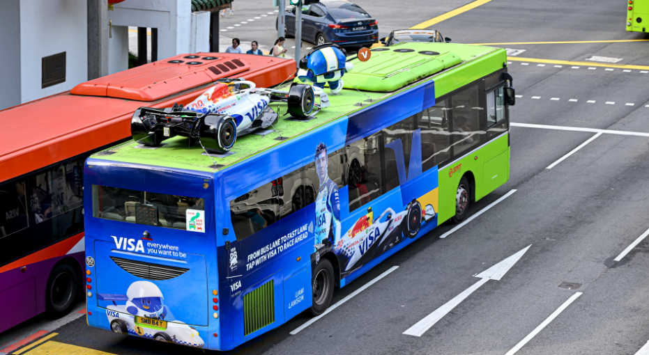 Custom 3D F1 racing car model sculpture displayed on top of a promotional city bus