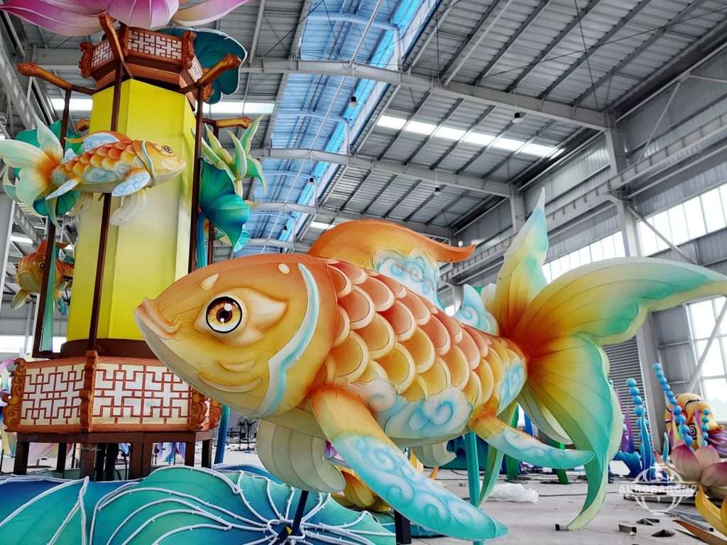 Close-up of giant rainbow koi fish lantern with detailed scales beside a rotating palace lantern in workshop display