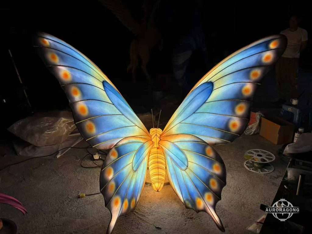 Custom illuminated blue butterfly lantern with orange spotted wings and golden body in a workshop