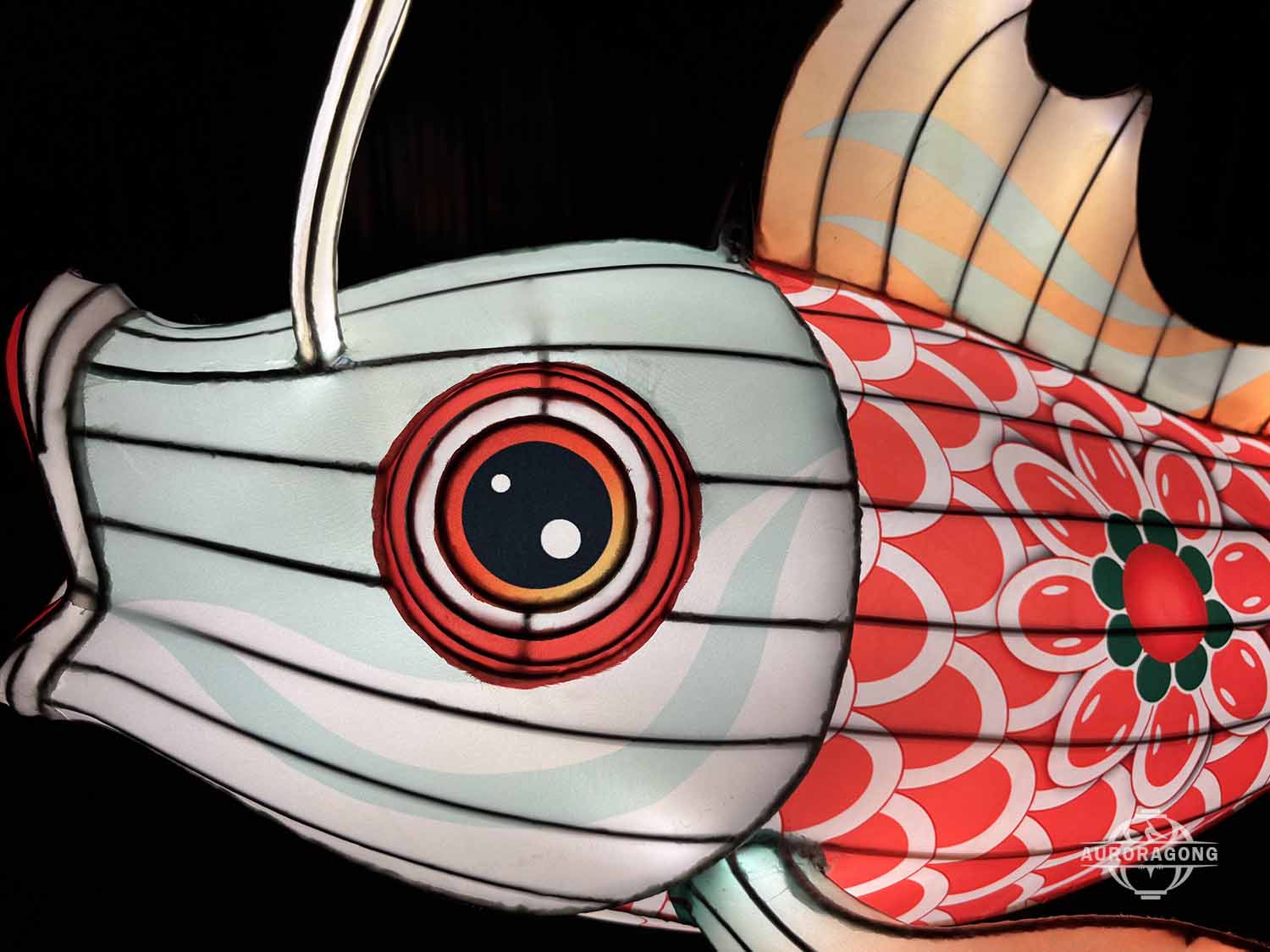 Close-up of illuminated carp lantern eye and red scales with green and orange fins at night