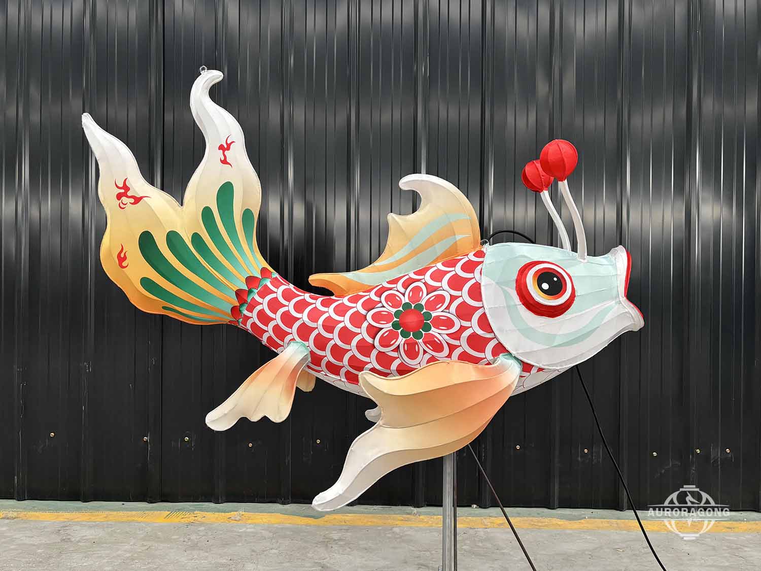 Side view of illuminated carp lantern with red and white scaled body and orange tail in workshop display