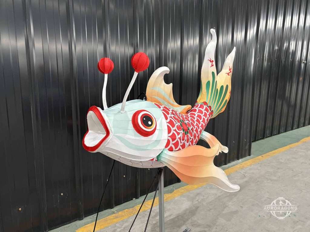 Front view of illuminated carp lantern with red barbels and open mouth in workshop display