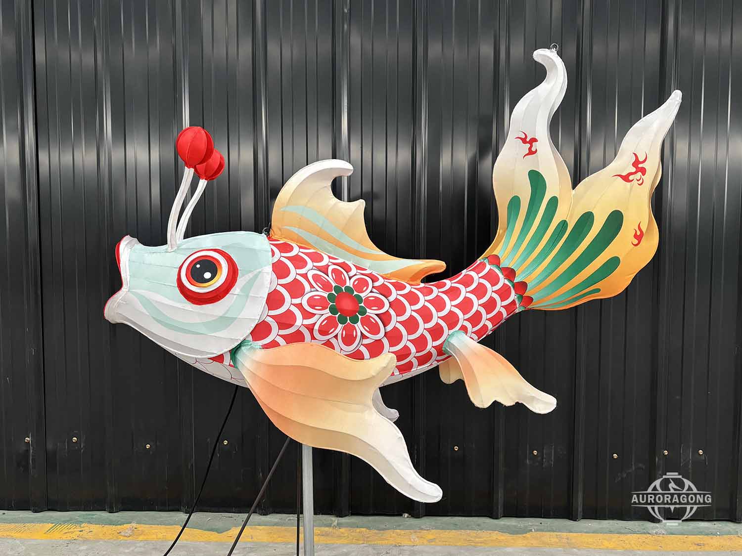 Custom illuminated carp lantern with red and green scaled body and orange fins in workshop display