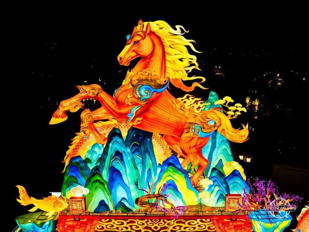 Giant illuminated dragon-horse lantern with golden dragon head on rainbow mountain waves at night