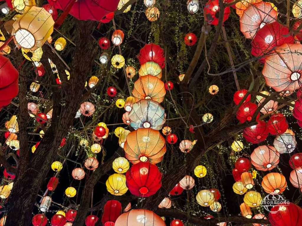 Real tree decorated with dense colorful traditional Chinese lanterns in red, orange, pink, and yellow for outdoor festival display