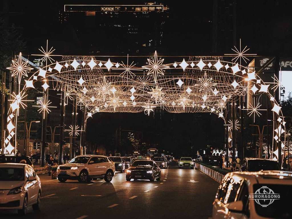 Custom illuminated white LED passage light arch with star and snowflake decorations across a city street at night