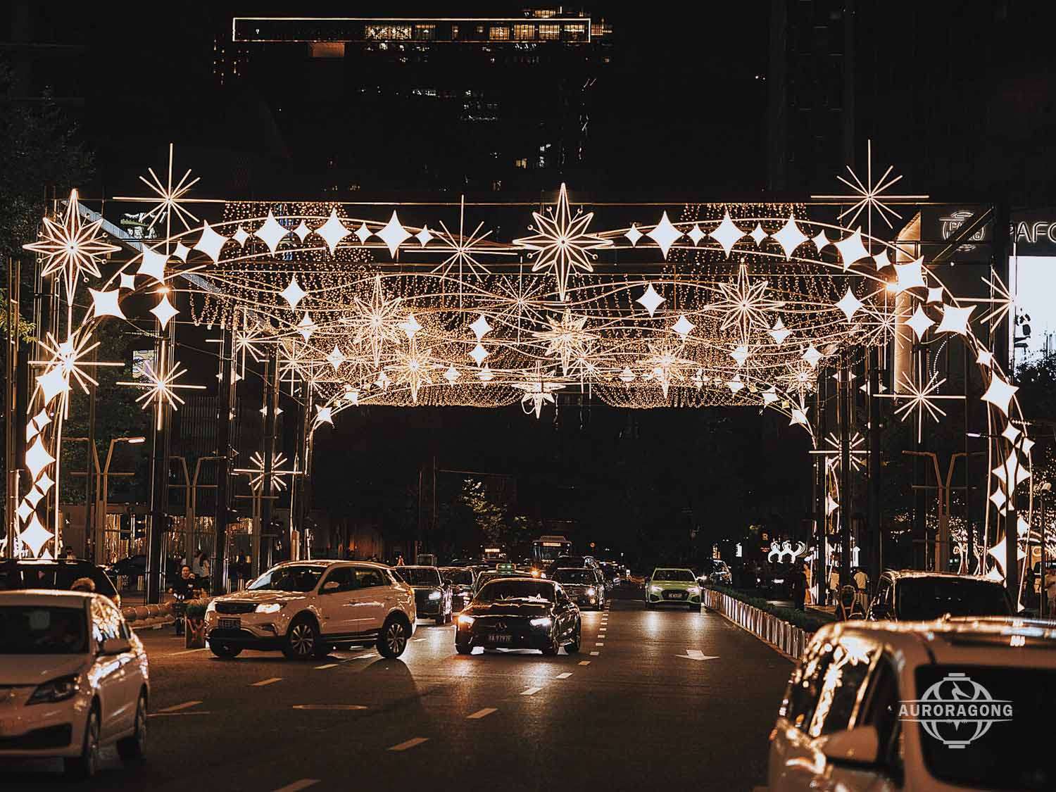 Custom illuminated white LED passage light arch with star and snowflake decorations across a city street at night