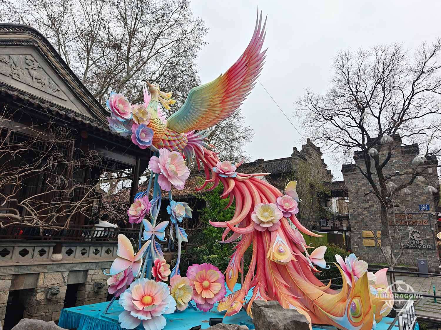 Colorful phoenix lantern with long tail feathers and flowers displayed during daytime