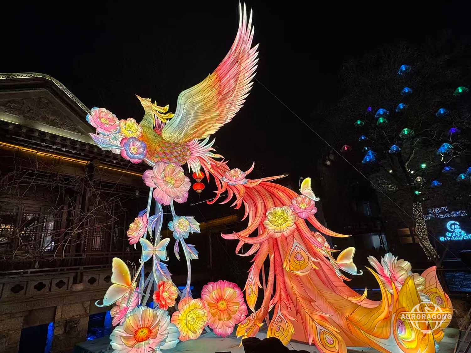 Giant illuminated phoenix lantern with flowing tail feathers and flowers at night