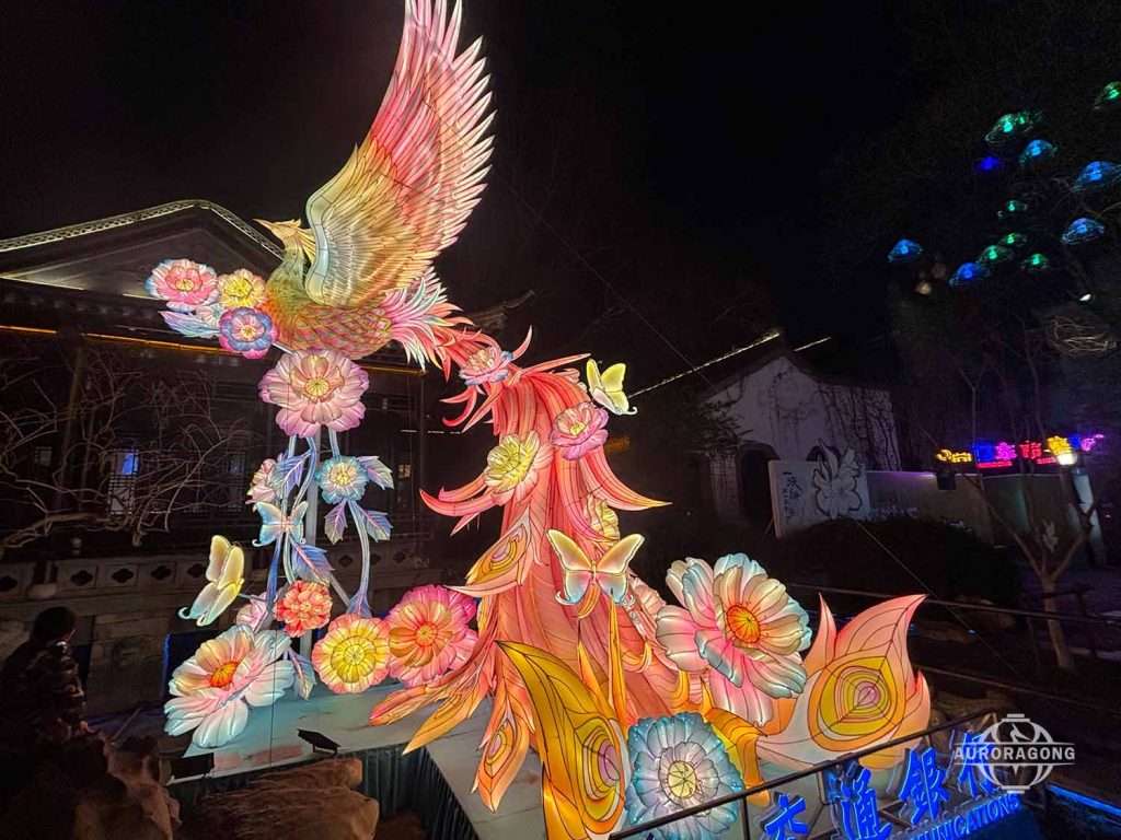 Custom illuminated pink and orange phoenix lantern with colorful flower decorations at traditional Chinese town night scene