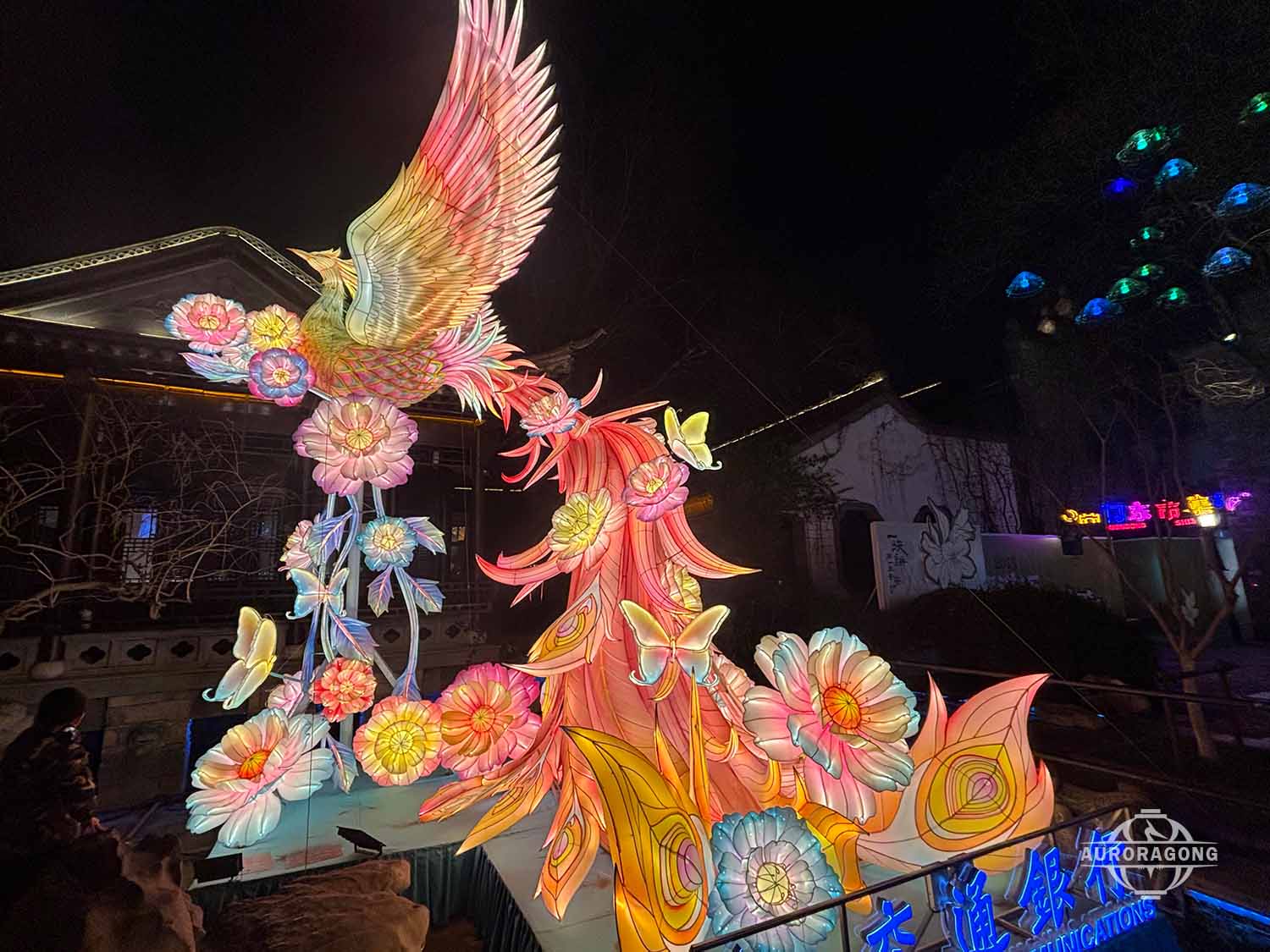 Custom illuminated pink and orange phoenix lantern with colorful flower decorations at traditional Chinese town night scene