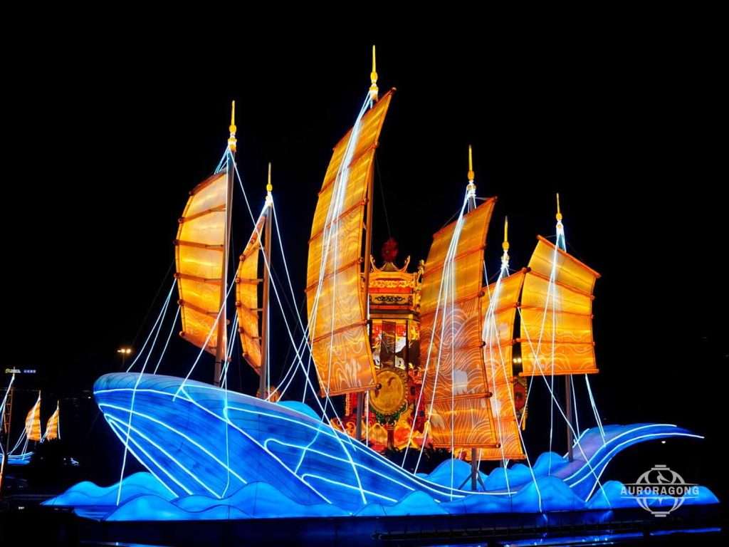 Large illuminated Chinese boat lantern with orange sails on blue waves at night