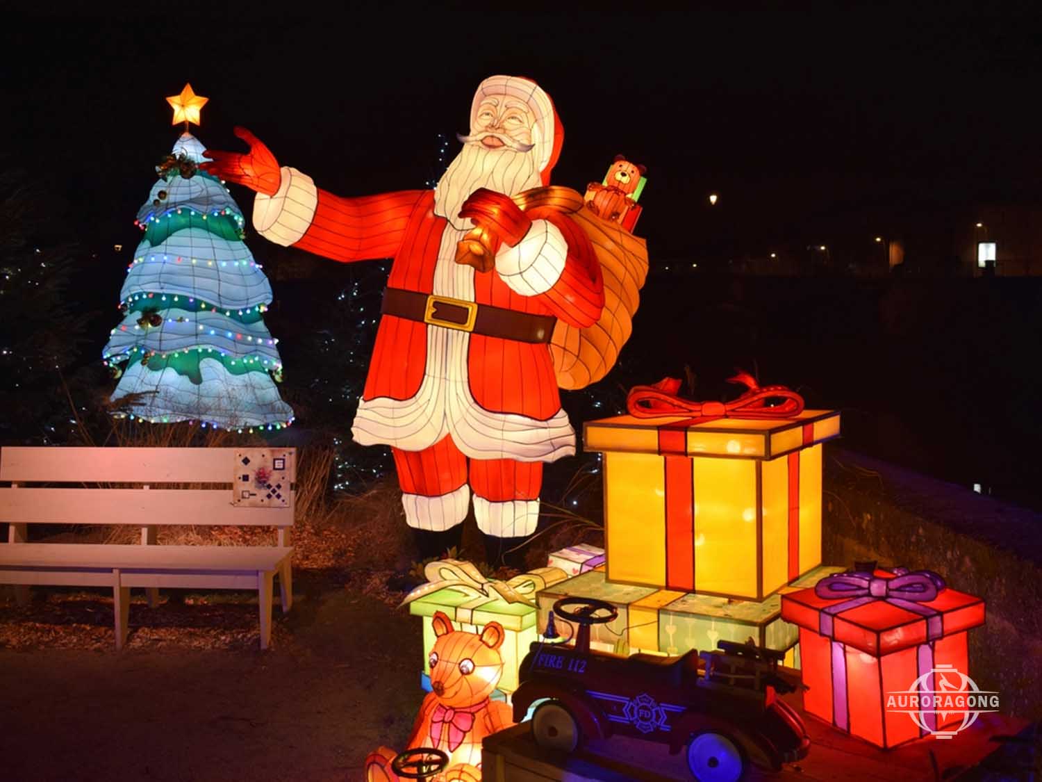 Outdoor Christmas scene with Santa Claus lantern, illuminated Christmas tree, and gift boxes