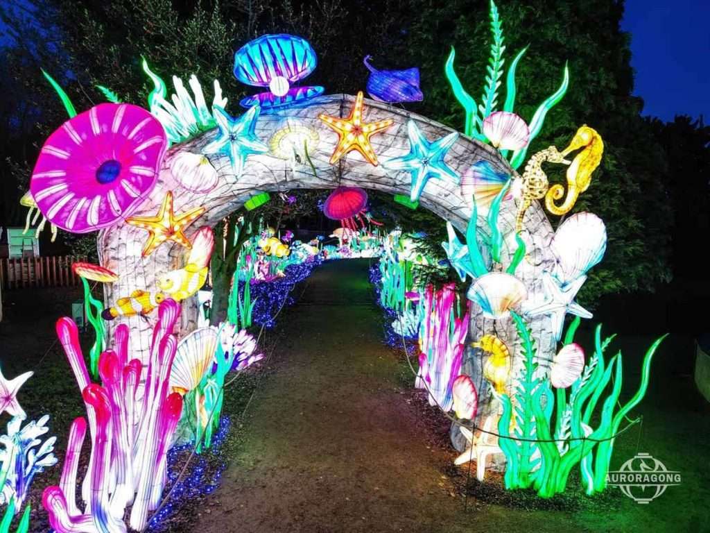 Walk-through illuminated ocean channel archway lantern with starfish, anemones, and shell decorations at dusk