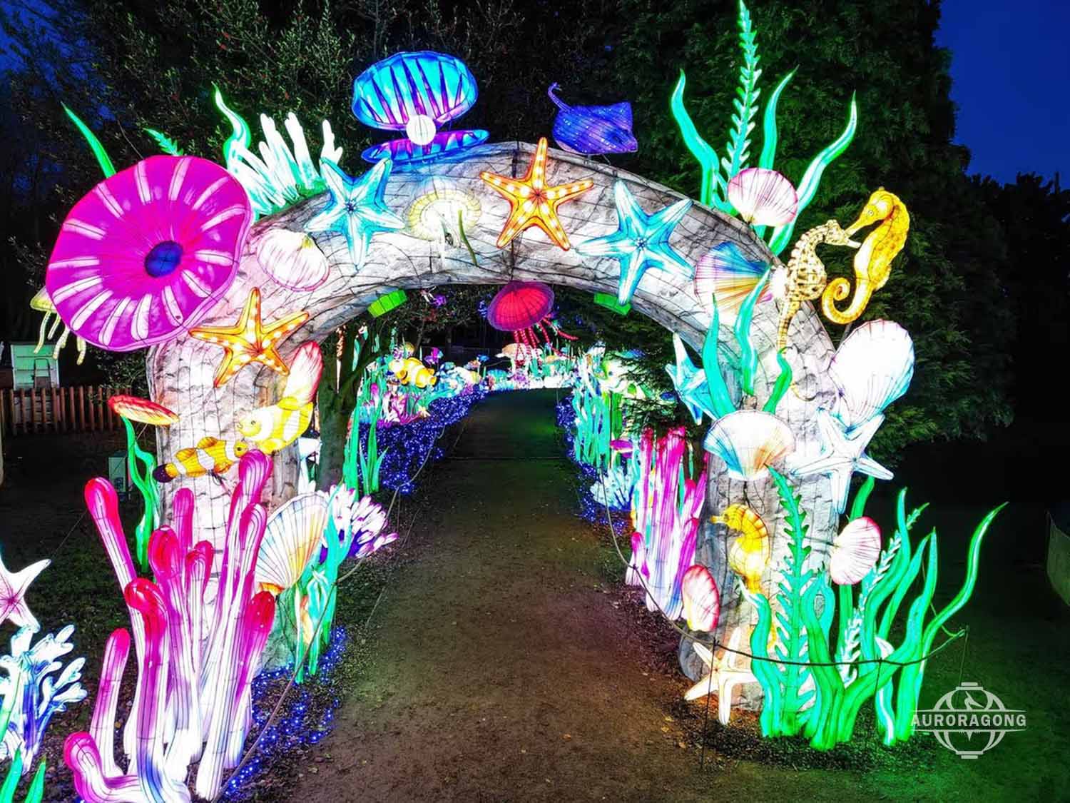 Walk-through illuminated ocean channel archway lantern with starfish, anemones, and shell decorations at dusk