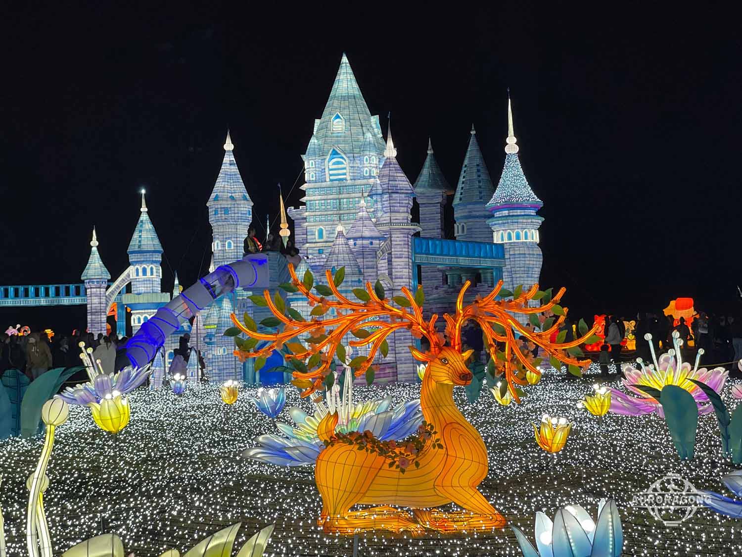 Illuminated ice castle with golden antlered deer and flower lanterns at a lumino city night festival