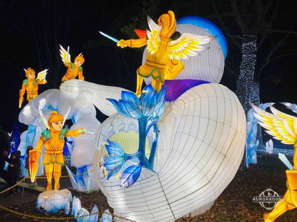 Illuminated angel and white whale lanterns with blue lotus flowers at a lumino city night festival