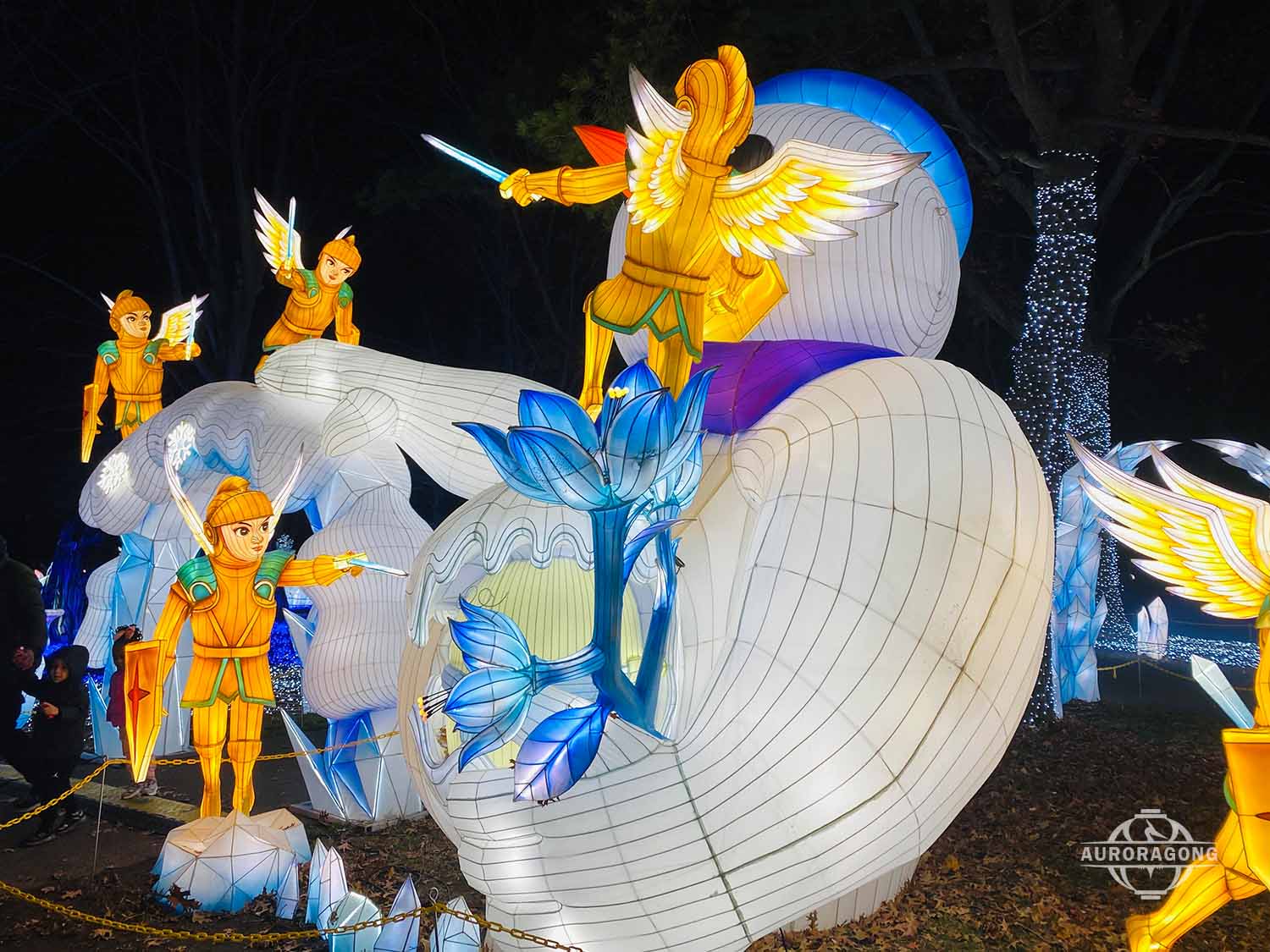 Illuminated angel and white whale lanterns with blue lotus flowers at a lumino city night festival