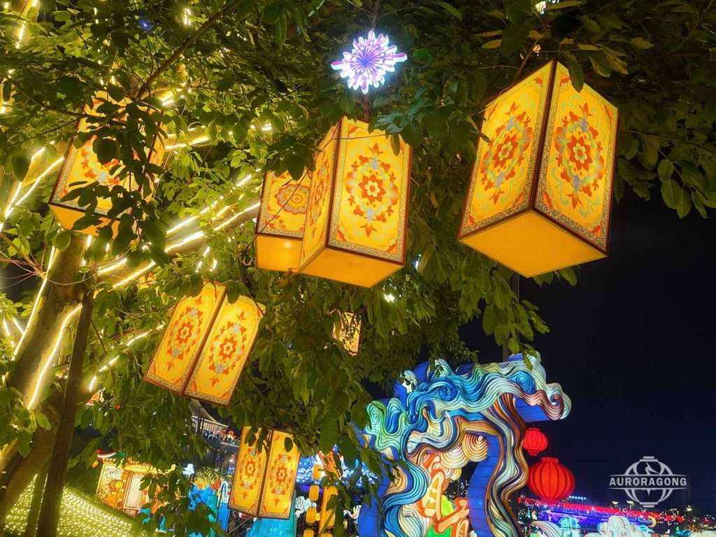 Tree with square yellow lanterns with red patterns hanging from branches at night