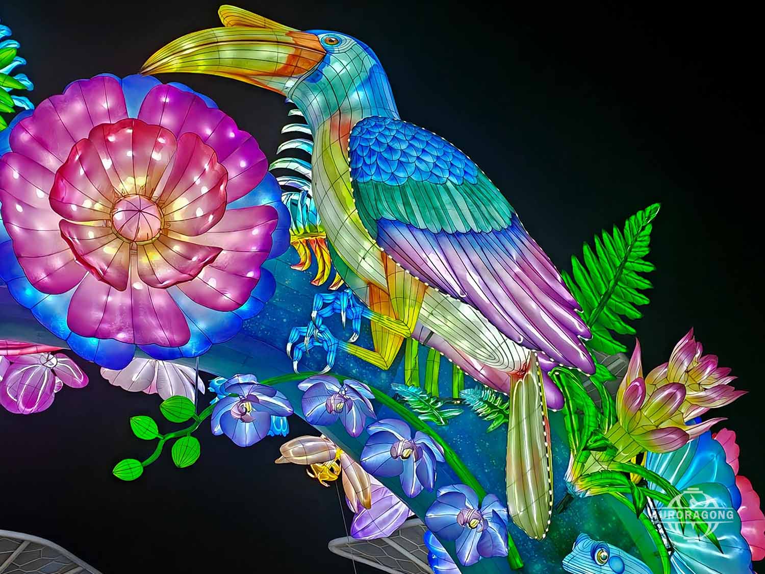 Colorful toucan and hummingbird lanterns with pink peony flowers and tropical leaves at a night festival