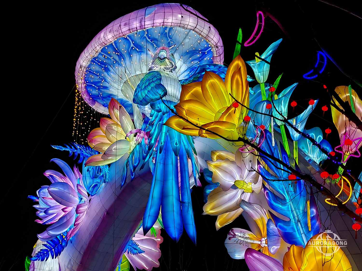Large illuminated whale lantern with jellyfish and colorful flowers in a night festival park display
