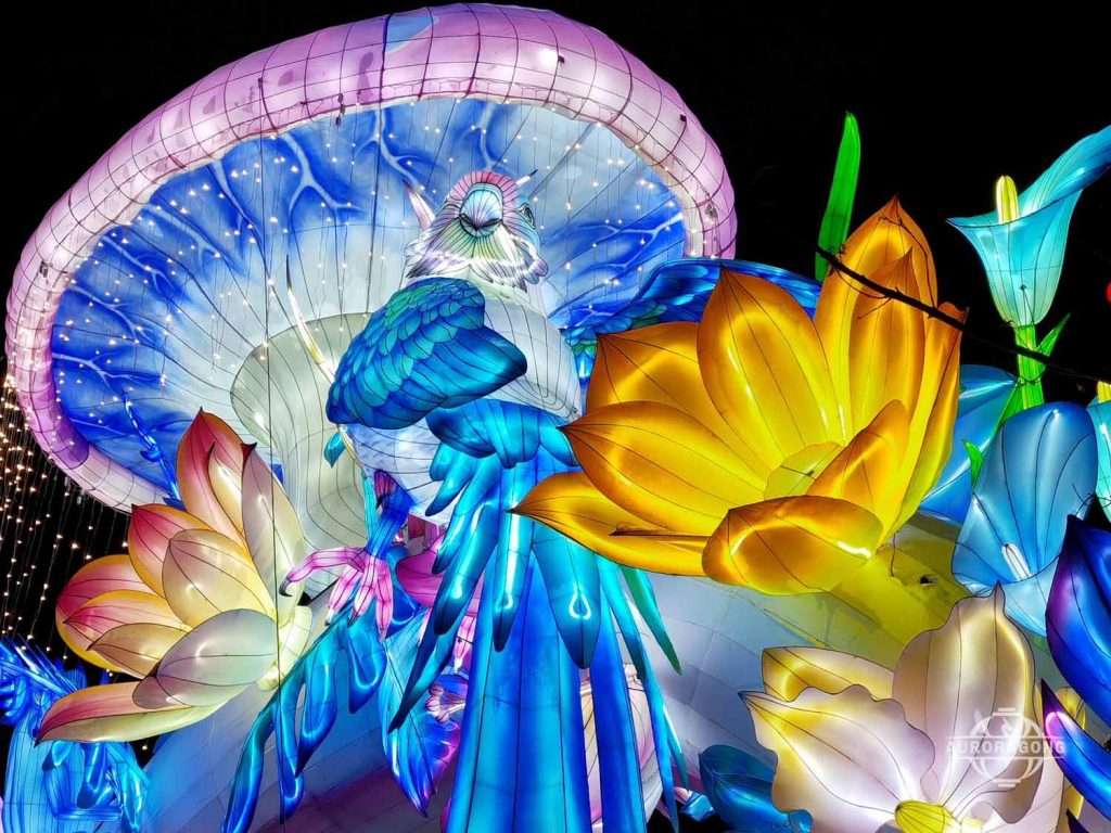 Illuminated jellyfish archway with yellow, blue, and pink flower lanterns at a night festival