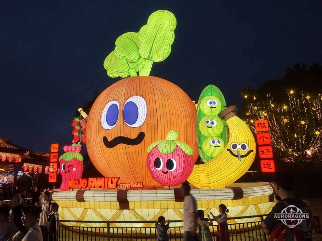 Cartoon carrot lantern with smiling face surrounded by cute fruit characters and a Chinese good luck symbol