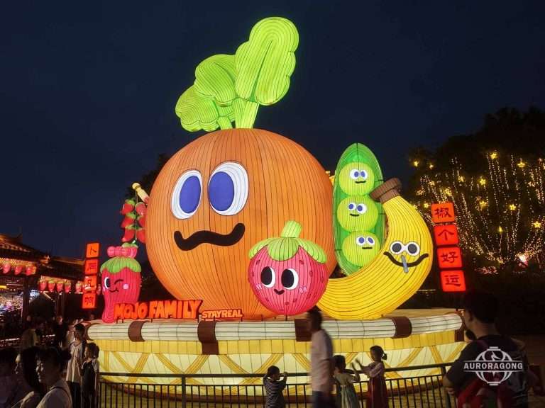 Cartoon carrot lantern with smiling face surrounded by cute fruit characters and a Chinese good luck symbol