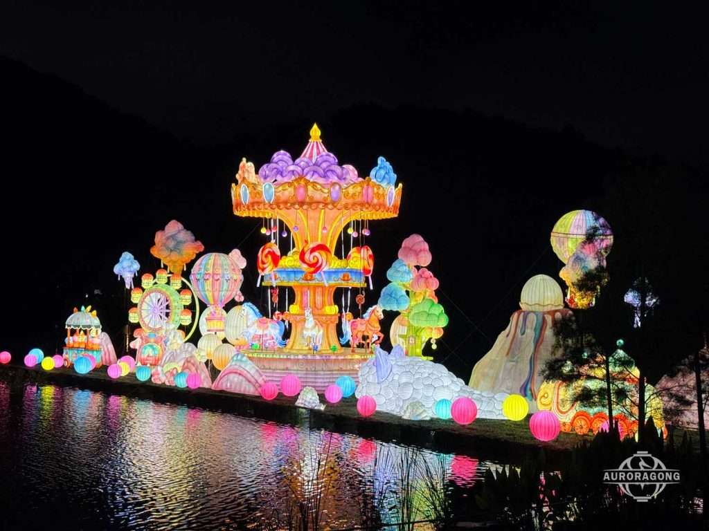 Large illuminated carousel lantern display at a theme park reflected in a lake at night