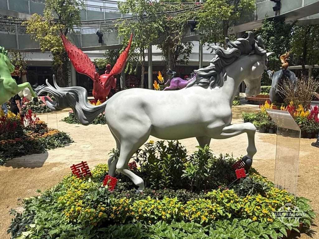White fiberglass horse sculpture in a galloping pose installed in a landscaped commercial plaza