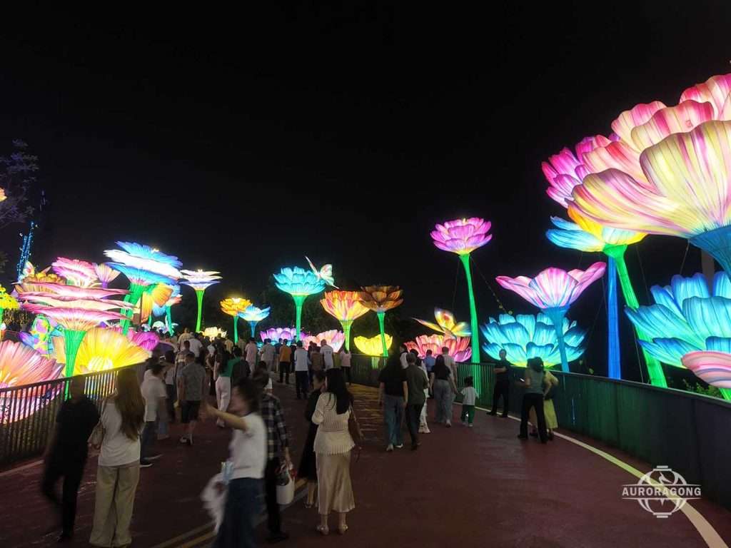 Colorful flower lantern walkway with visitors among giant glowing blooms at night