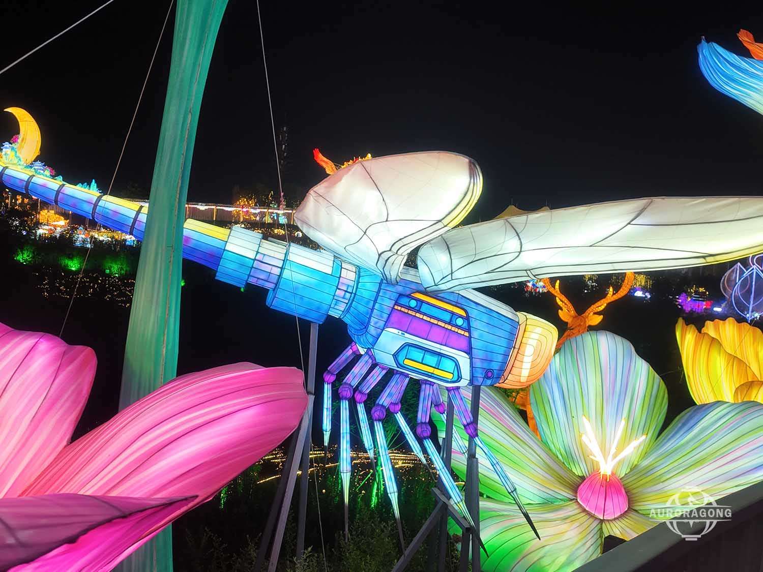 Close-up of an illuminated dragonfly lantern surrounded by colorful flower petals at a night festival walkway