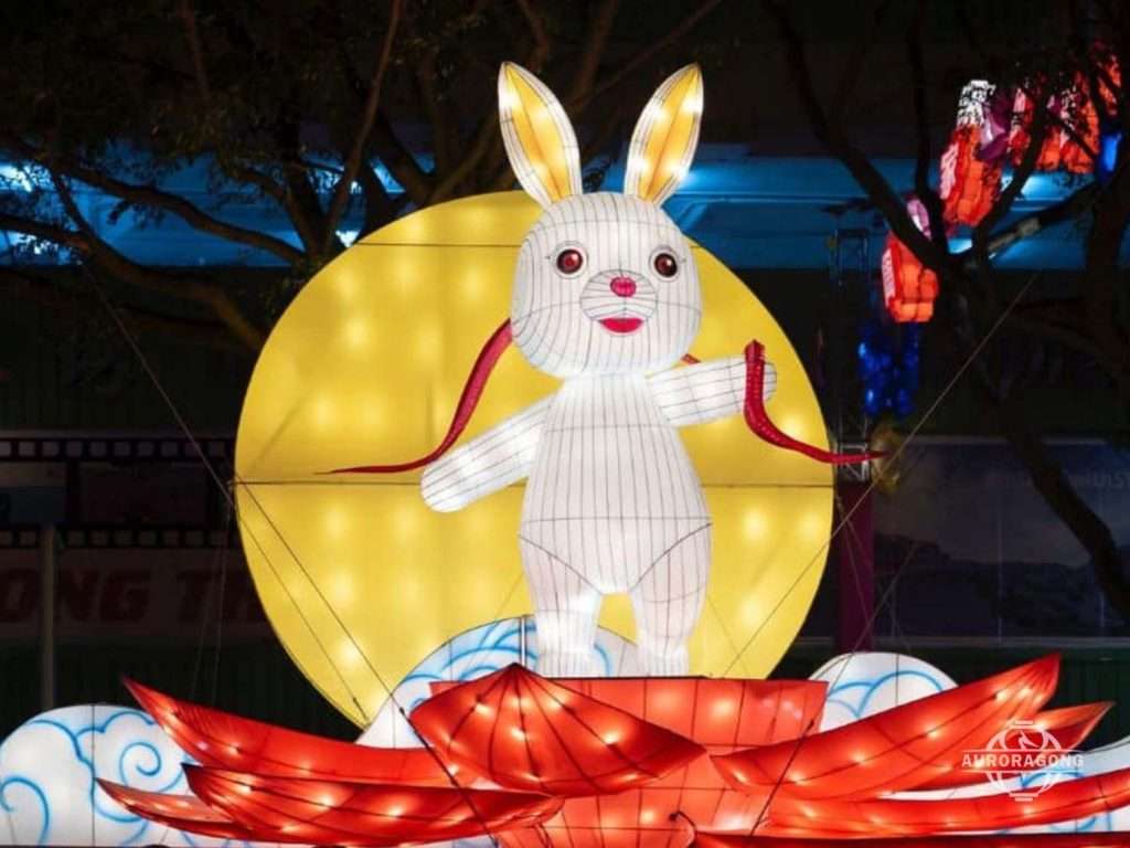 White rabbit lantern in front of a glowing moon lantern with red lotus at a Mid-Autumn festival display