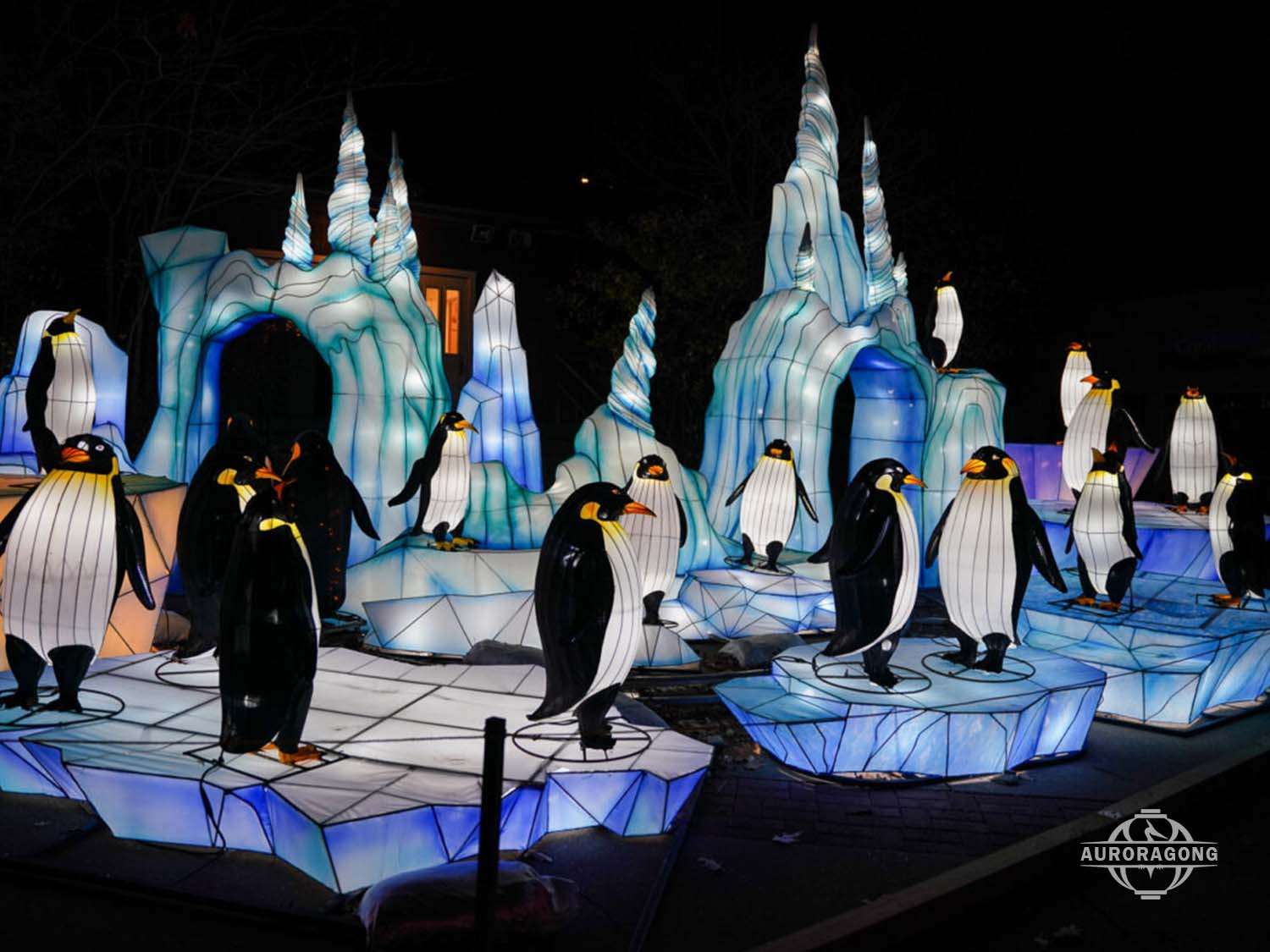Group of illuminated penguin lanterns displayed in front of blue-lit iceberg scenery at night