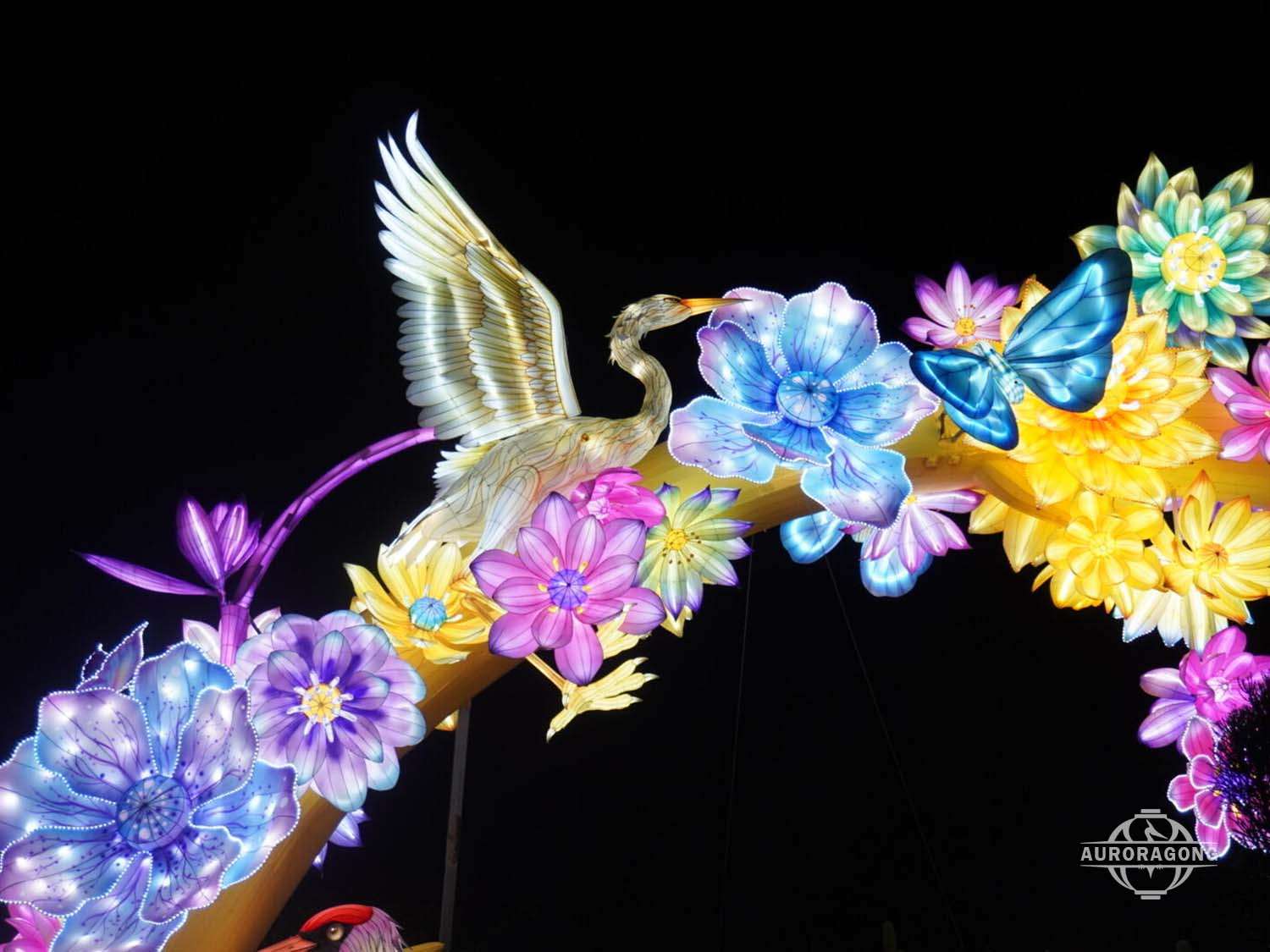 Single white crane with spread wings among colorful flowers in a flower arch lantern archway