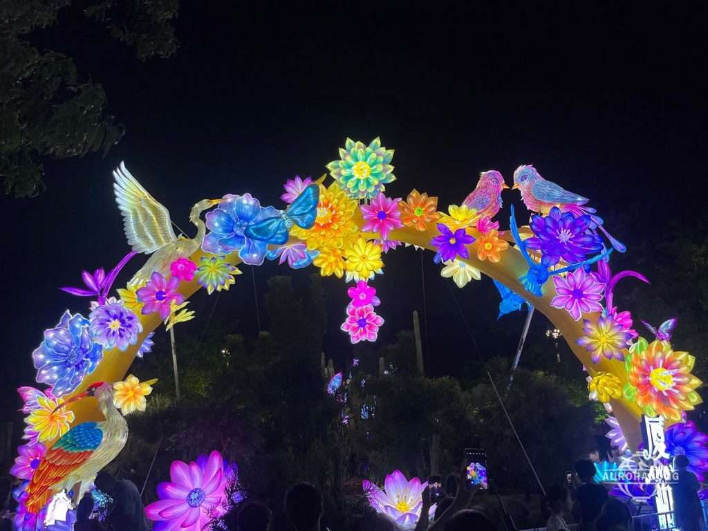 Multiple illuminated white cranes and colorful flowers forming a flower arch lantern archway at night