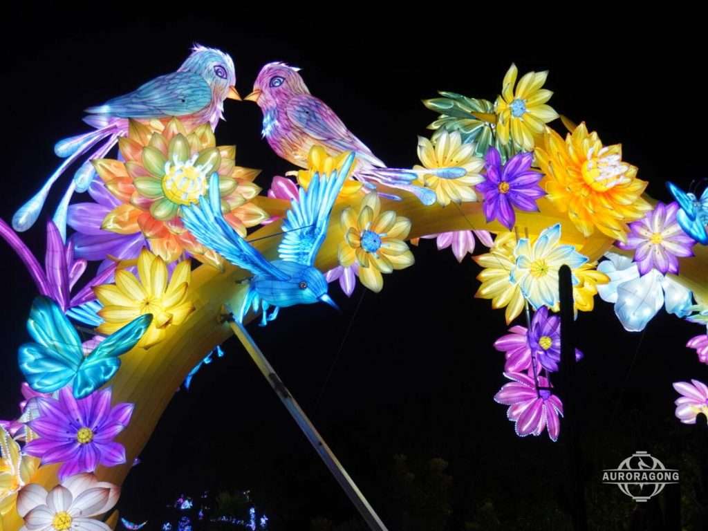 Two illuminated songbirds perched among colorful flowers in a flower arch lantern archway