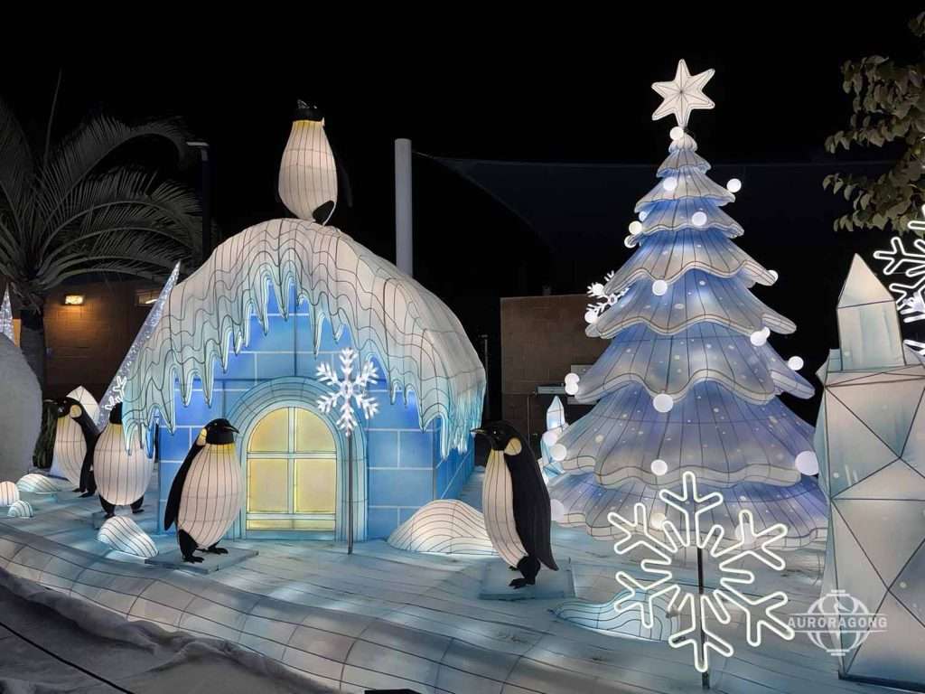 Illuminated igloo lantern with penguins and a large white Christmas tree at an outdoor winter lantern festival display