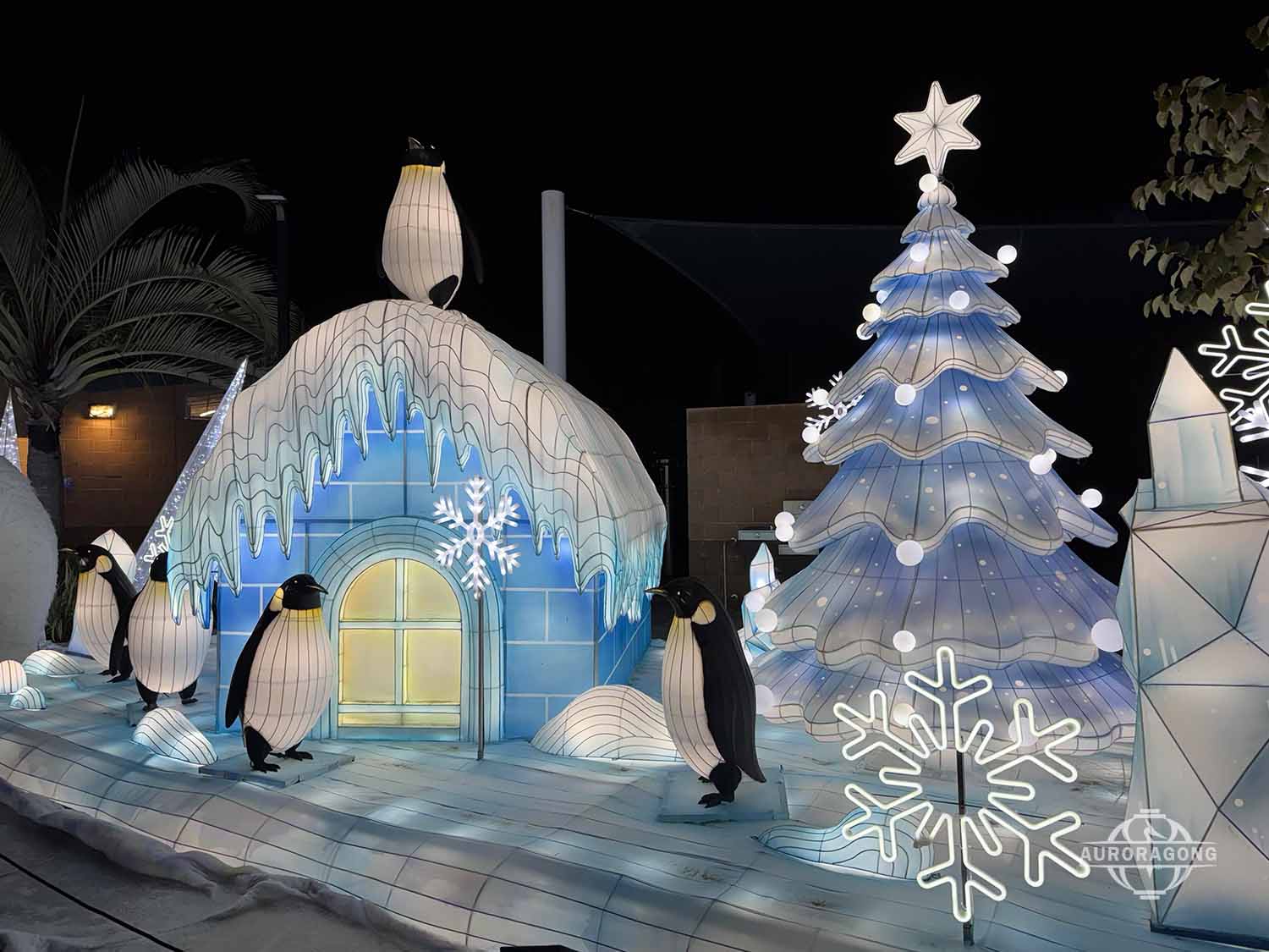 Illuminated igloo lantern with penguins and a large white Christmas tree at an outdoor winter lantern festival display