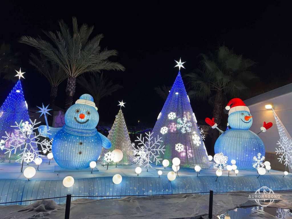 Two illuminated snowman lanterns with Christmas trees and snowflake decorations at an outdoor winter lantern festival