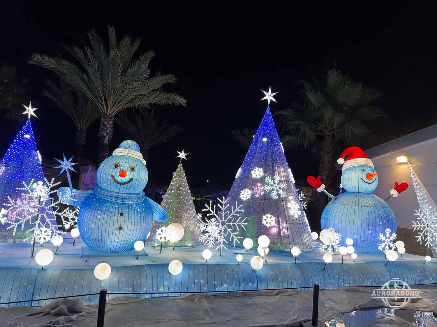 Two illuminated snowman lanterns with Christmas trees and snowflake decorations at an outdoor winter lantern festival