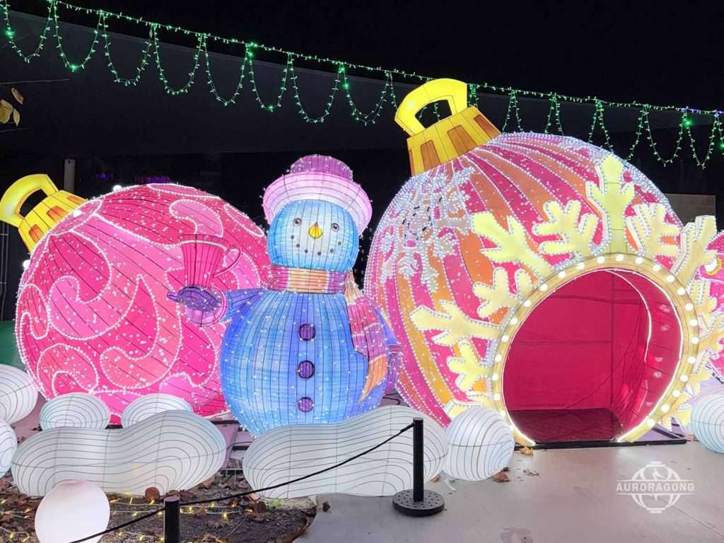 Pink polka-dot hat snowman lantern beside a walk-through Christmas bauble lantern at an outdoor winter lantern festival