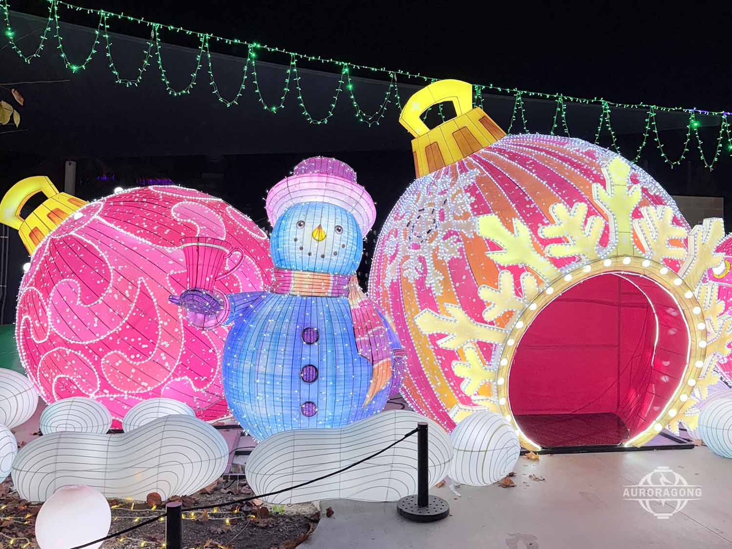 Pink polka-dot hat snowman lantern beside a walk-through Christmas bauble lantern at an outdoor winter lantern festival